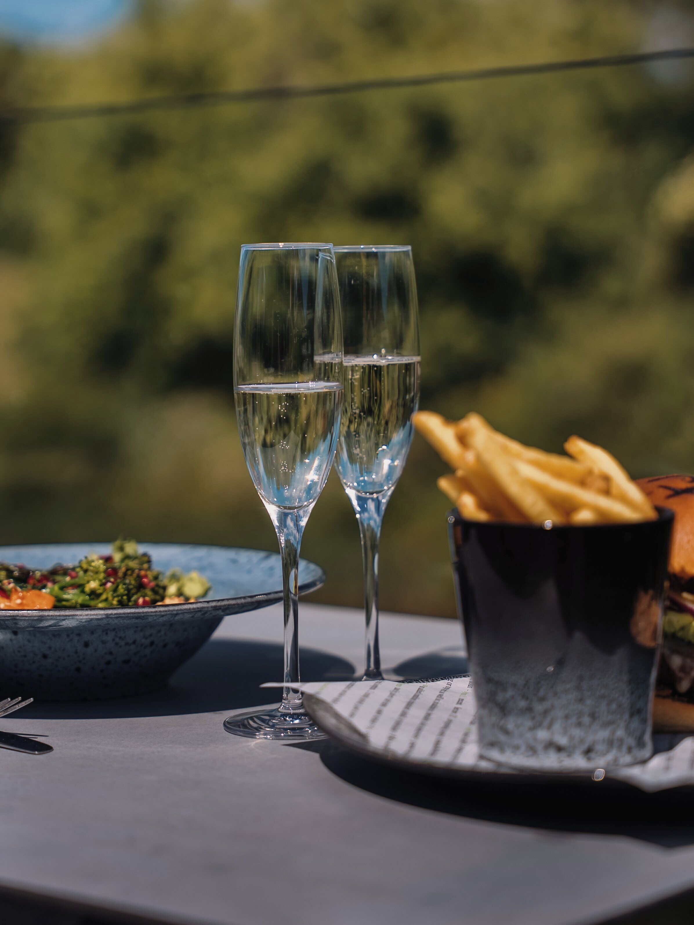 Deux verres d’eau sur une table, avec une assiette de nourriture et un panier de frites.
