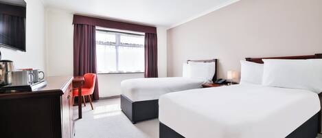 A hotel room with two beds, a desk with a chair, a TV, and a window with curtains.
