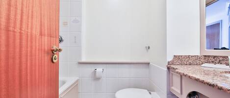 Et badeværelse med et hvidt toilet, en vask med bordplade i granit og et spejl over vasken.