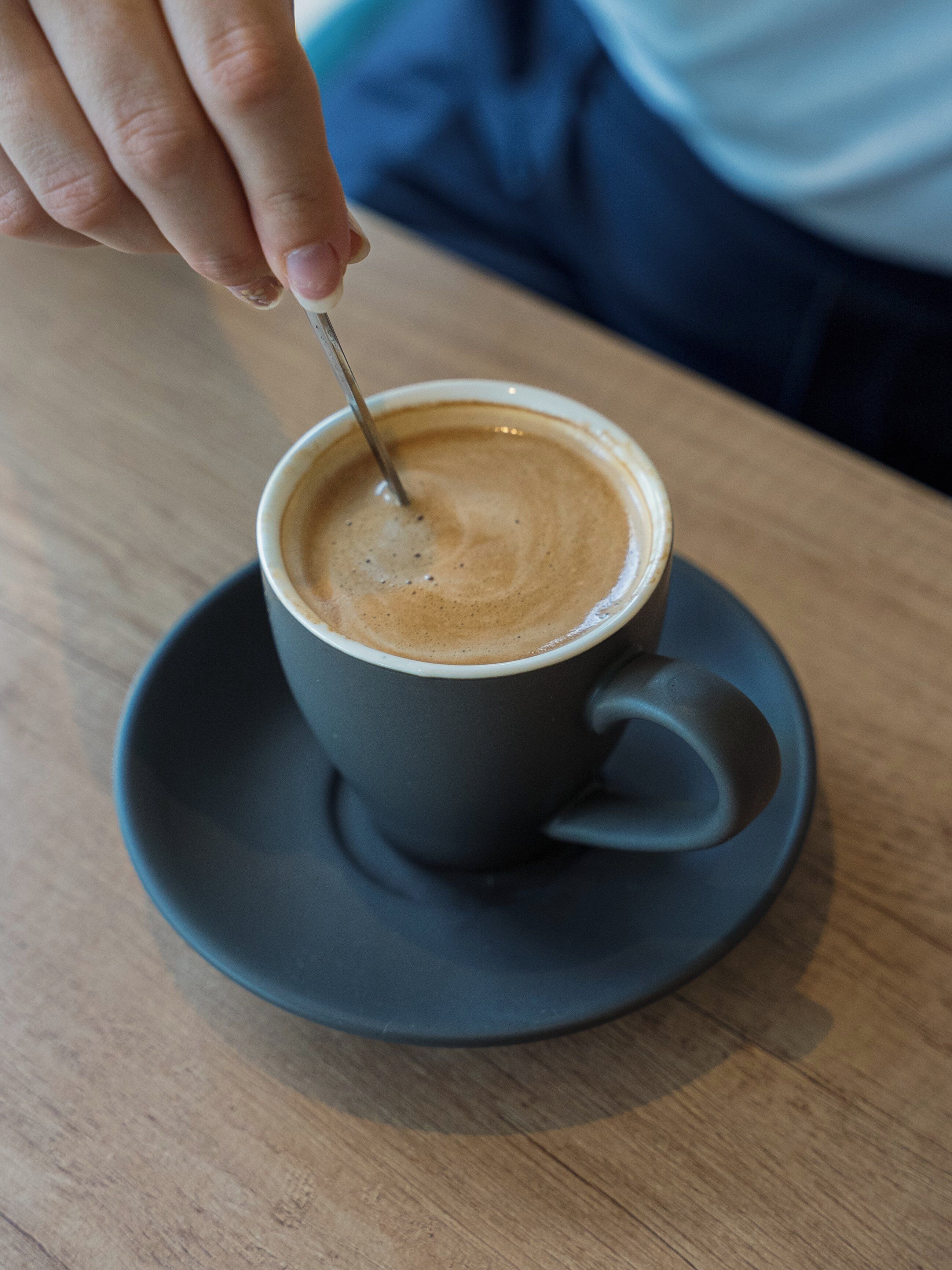A hand stirring a cup of coffee on a saucer.