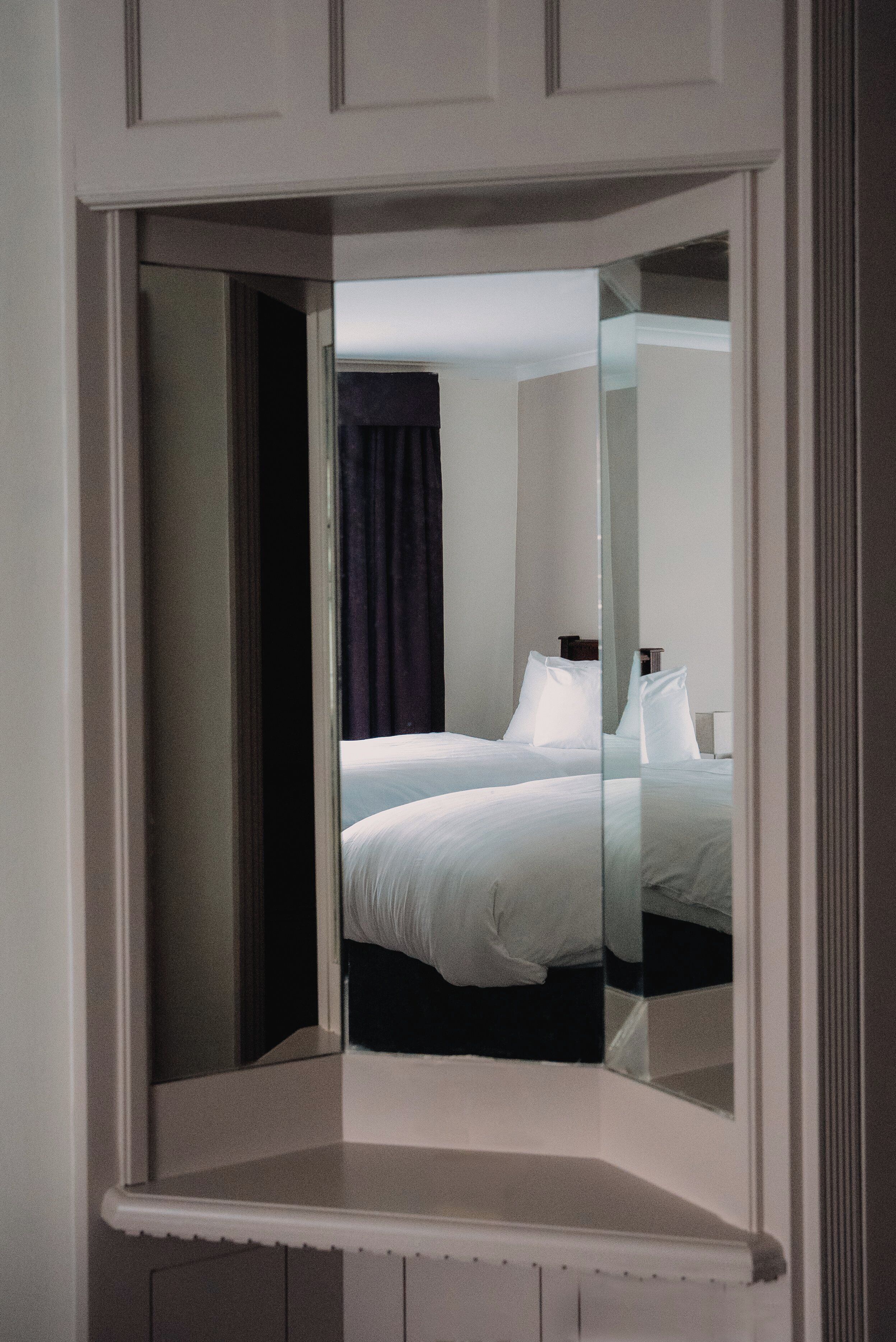 A hotel room with a bed, a nightstand, and a mirror reflecting the room.
