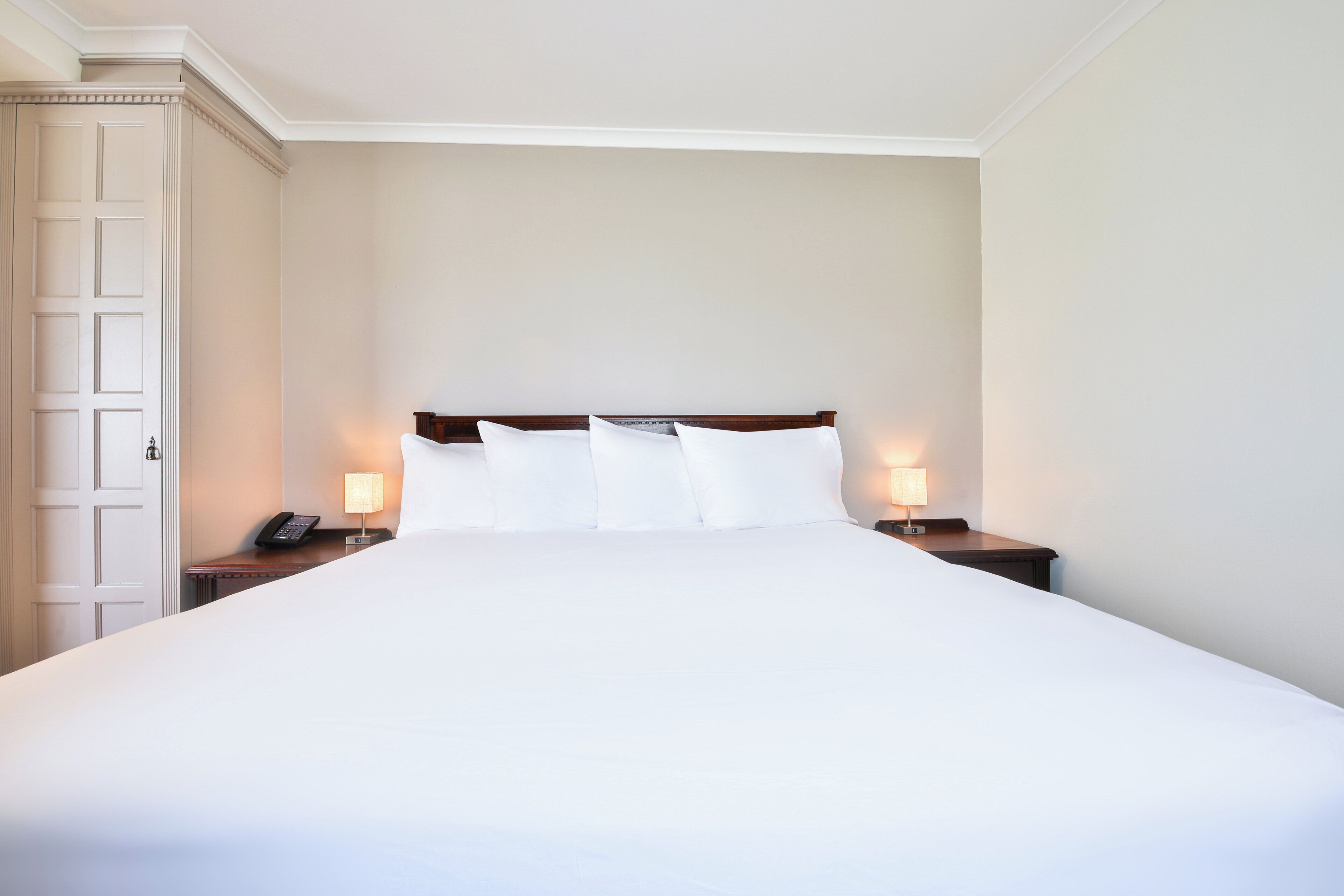 Una cama grande con cabecera de madera, dos mesitas de noche con lámparas y una puerta a la izquierda.