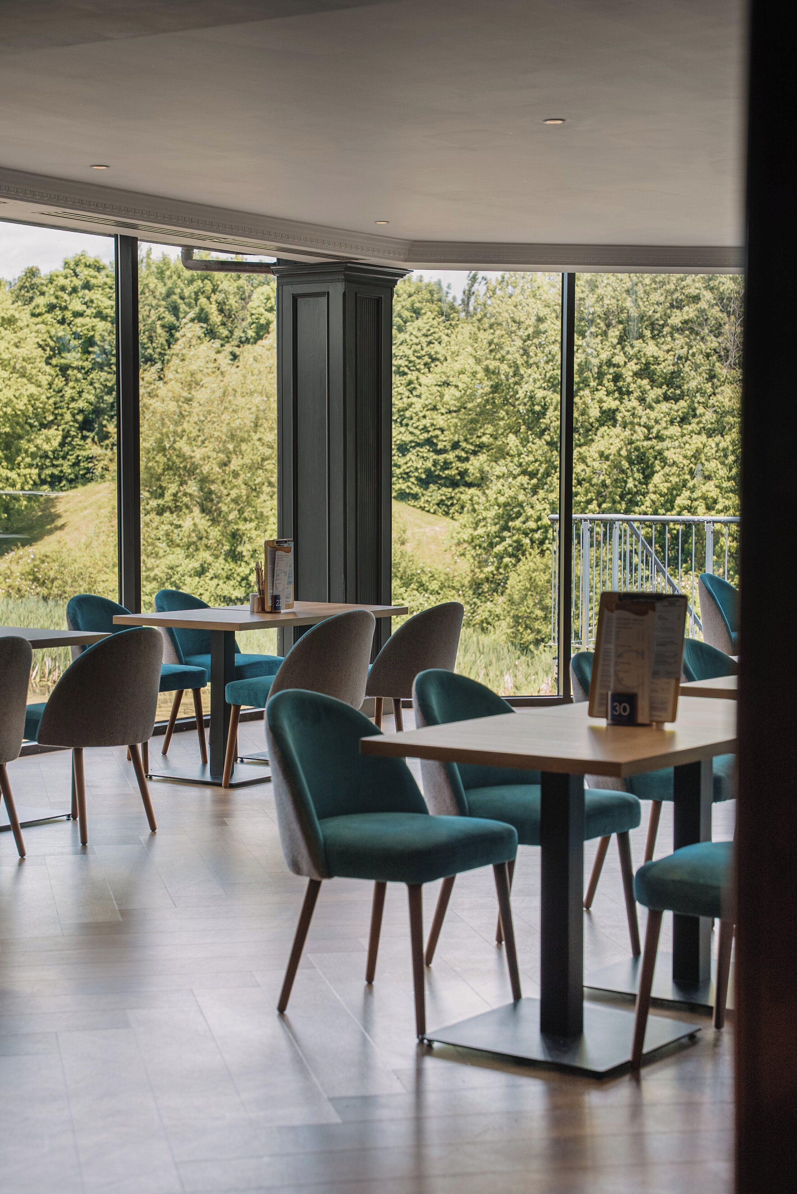 A modern dining area with large windows, wooden flooring, and teal chairs.