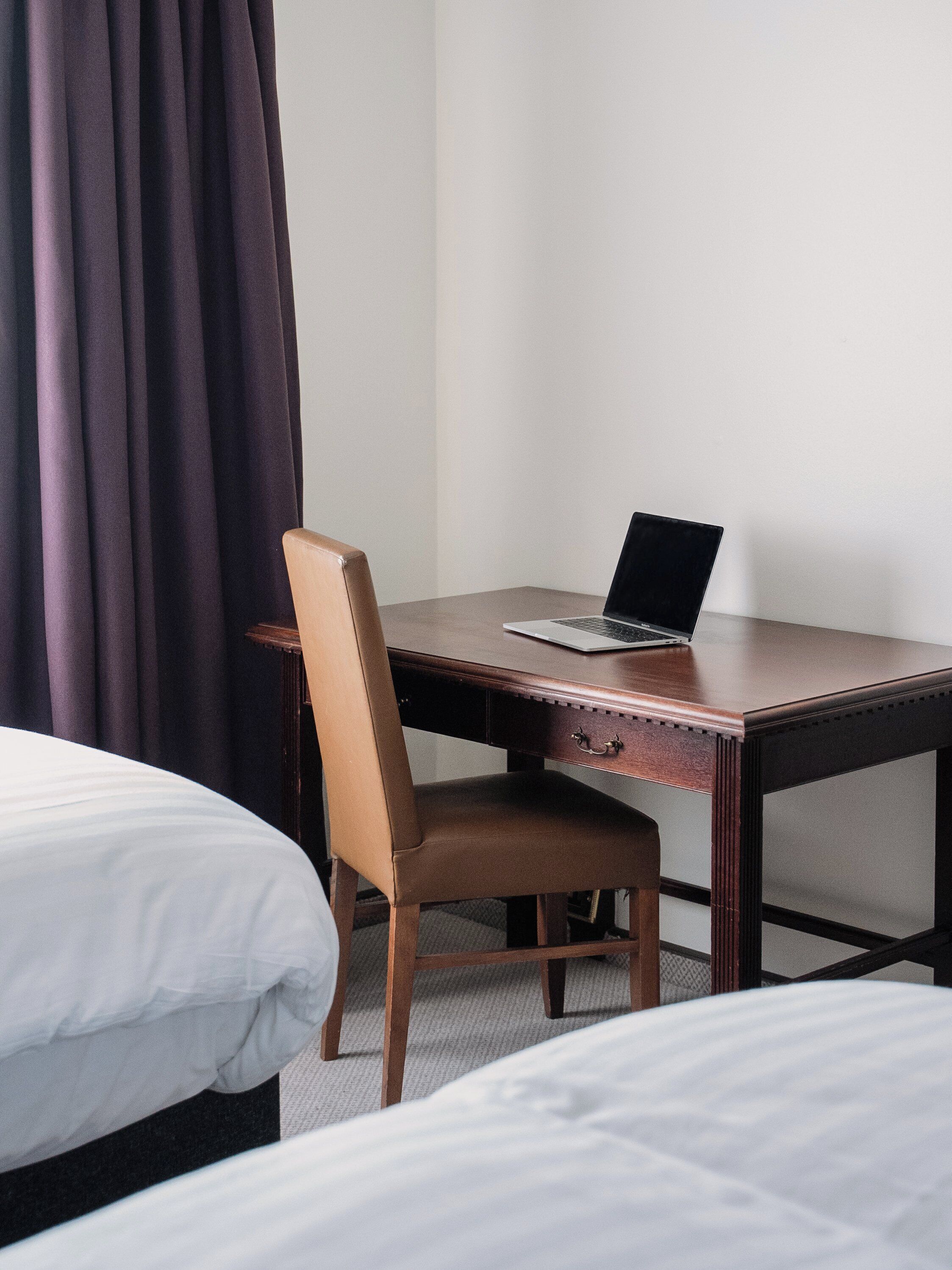 Ein Hotelzimmer mit einem Holztisch, einem Laptop, einem Stuhl und zwei Betten.