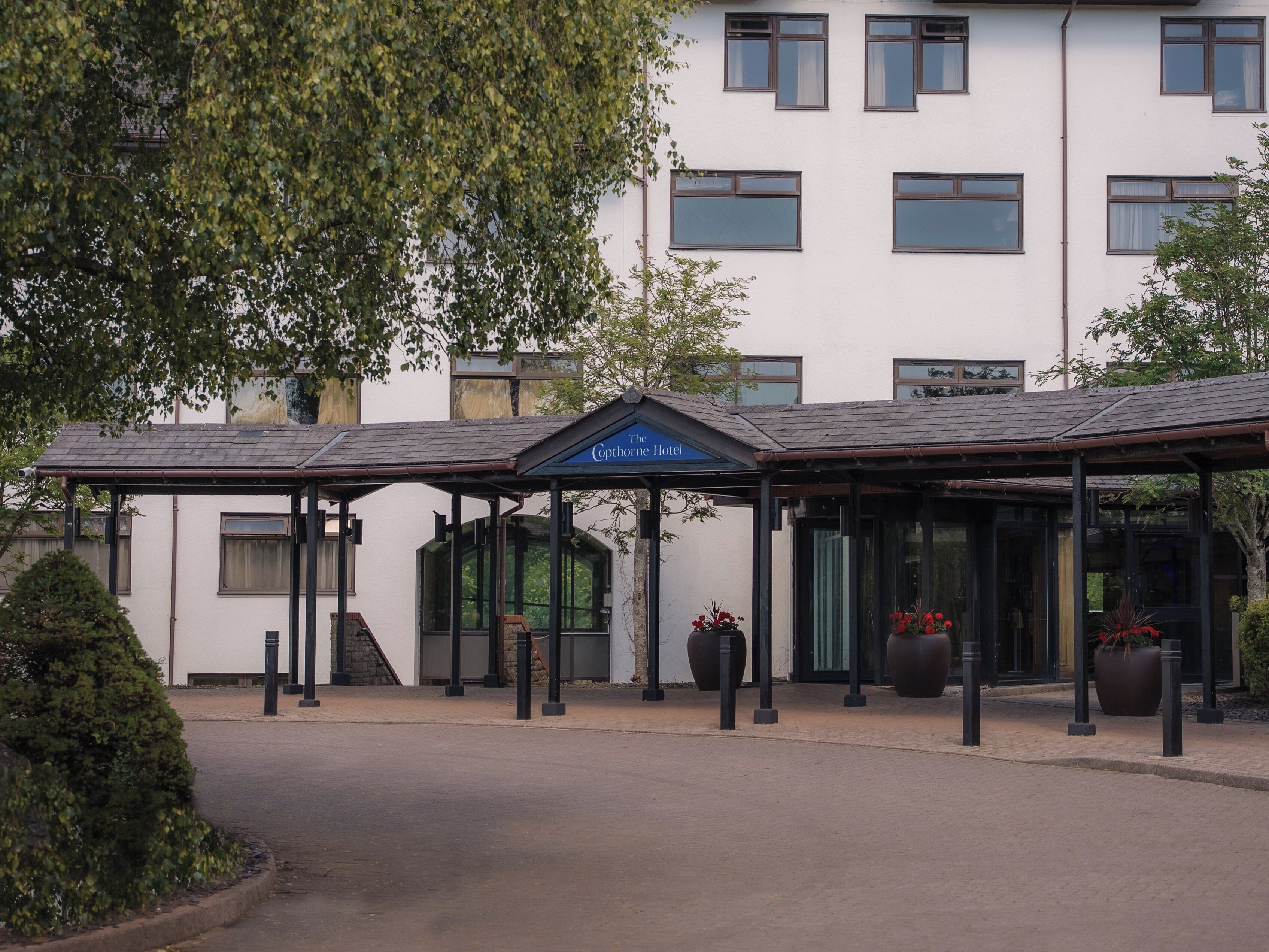 A hotel entrance with a covered waiting area, large windows, and potted plants.
