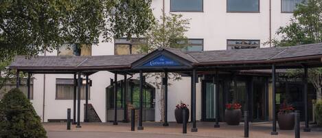 A hotel entrance with a covered waiting area, large windows, and potted plants.