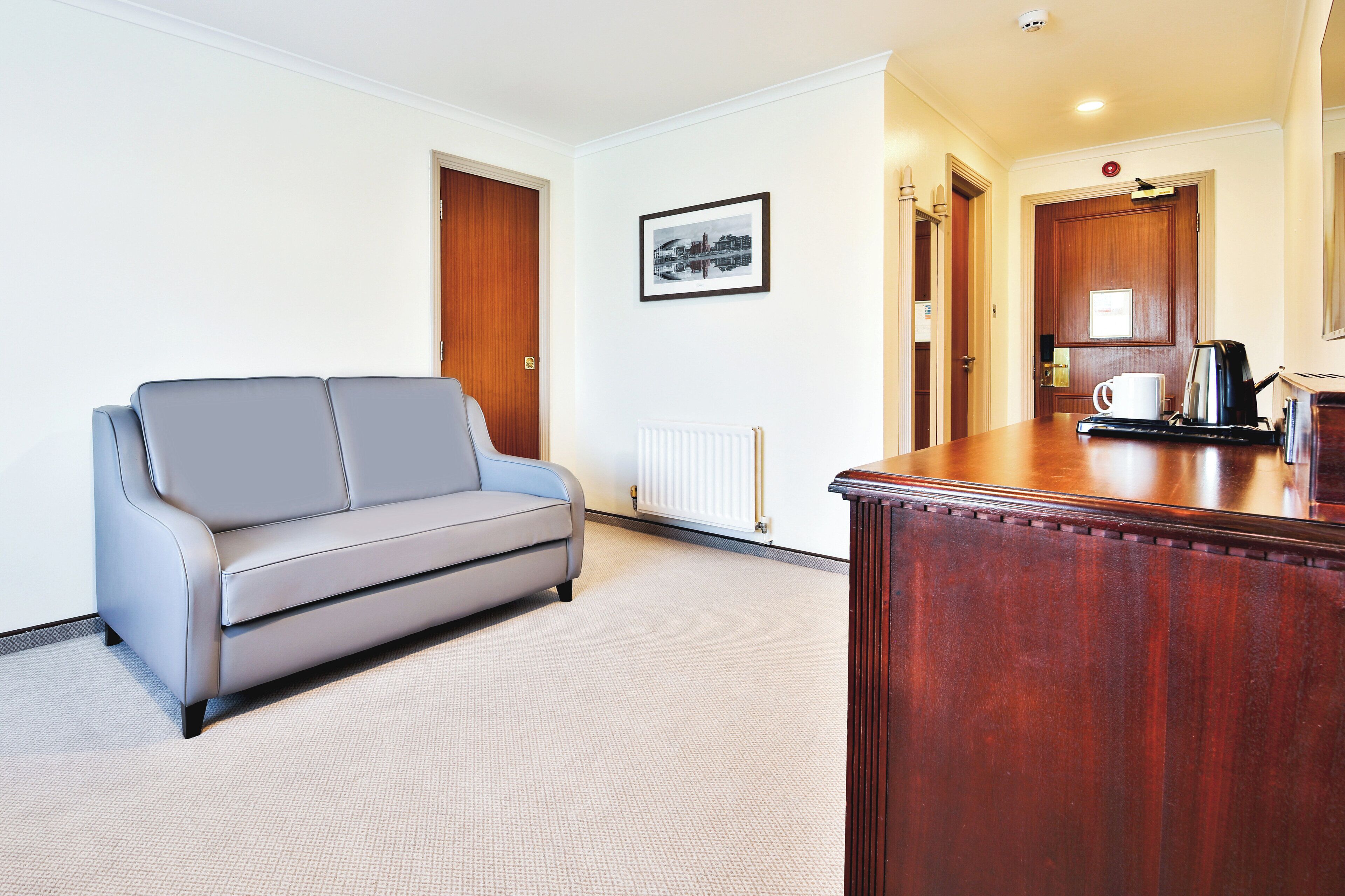 A modern hotel room with a grey sofa, a wooden desk, and a framed picture on the wall.
