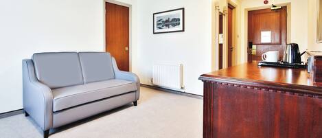 A modern hotel room with a grey sofa, a wooden desk, and a framed picture on the wall.