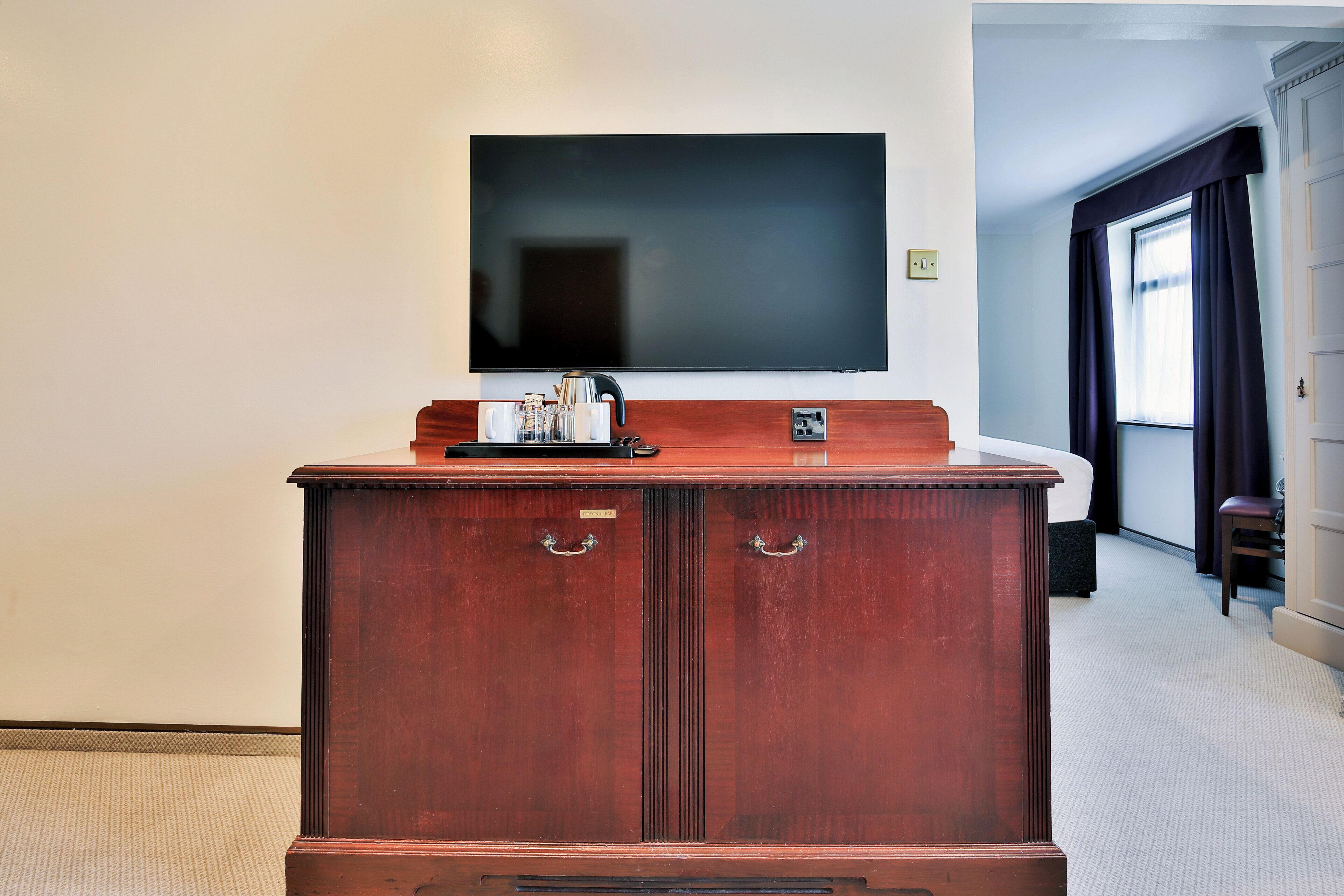 Un mueble de madera con un televisor de pantalla plana montado encima, una tetera y una bandeja con tazas y un plato pequeño.