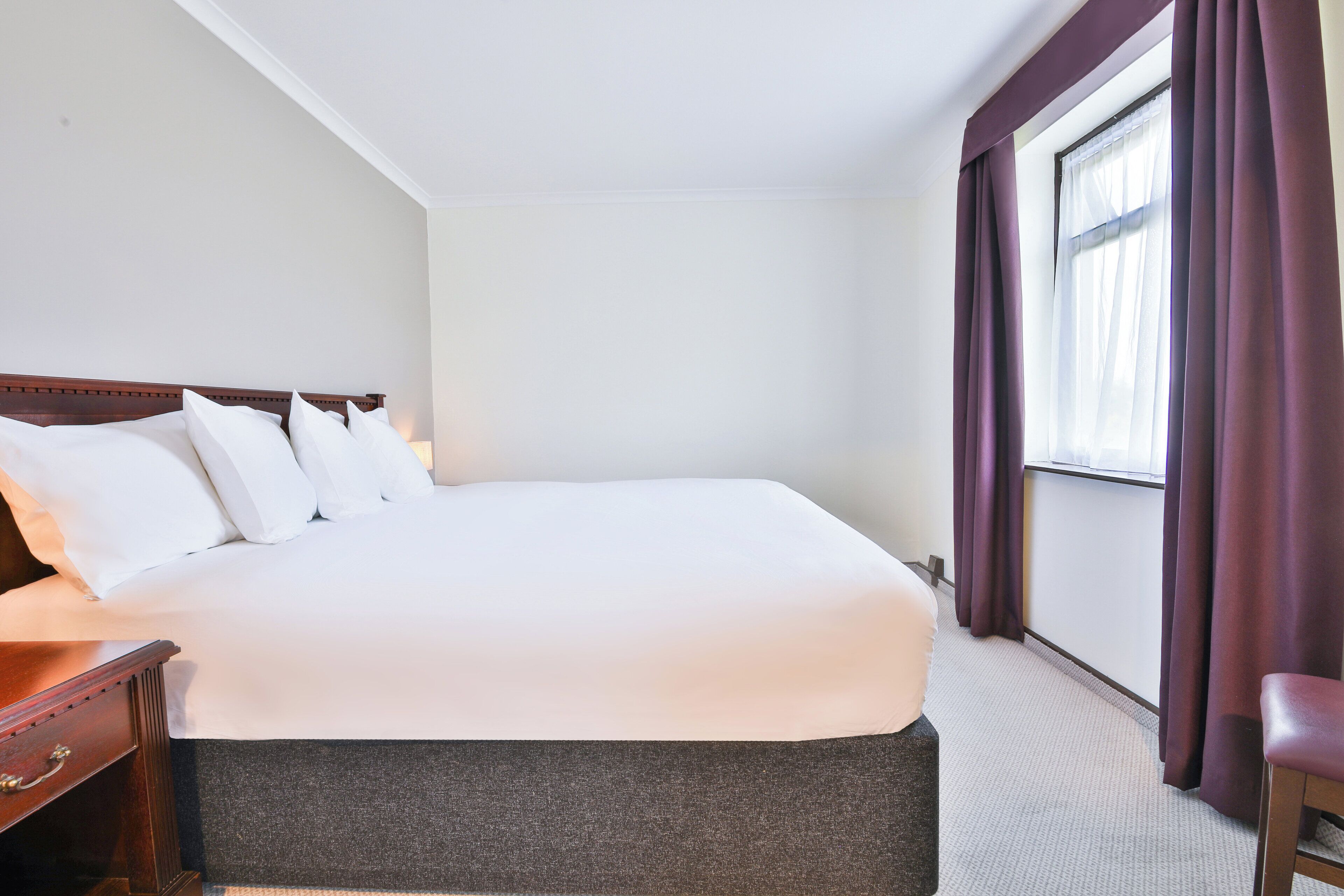 Une chambre d’hôtel avec un grand lit, une table de chevet en bois, un bureau et une fenêtre avec des rideaux.