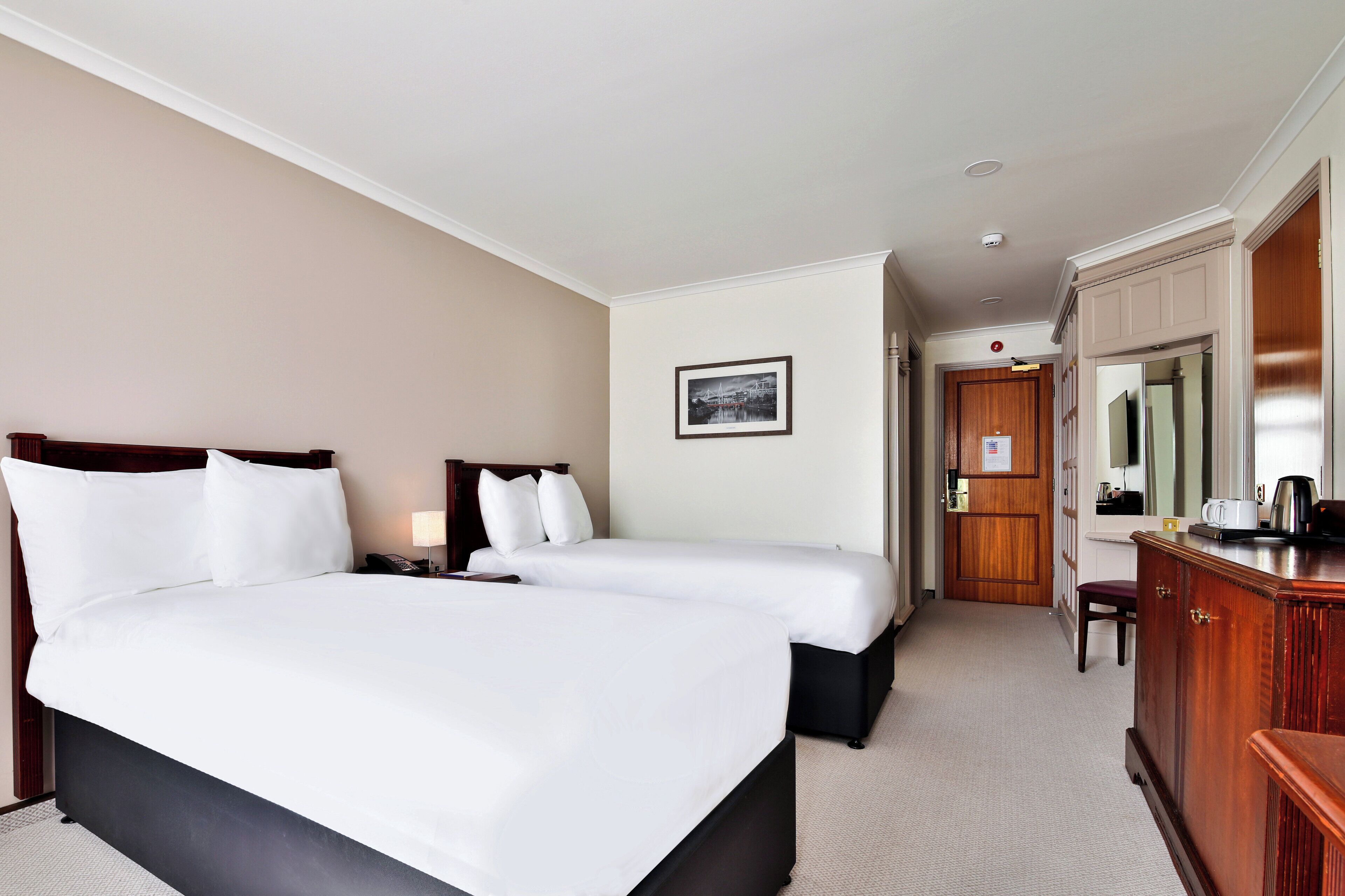 A hotel room with two beds, a wooden dresser, a desk, and a chair.
