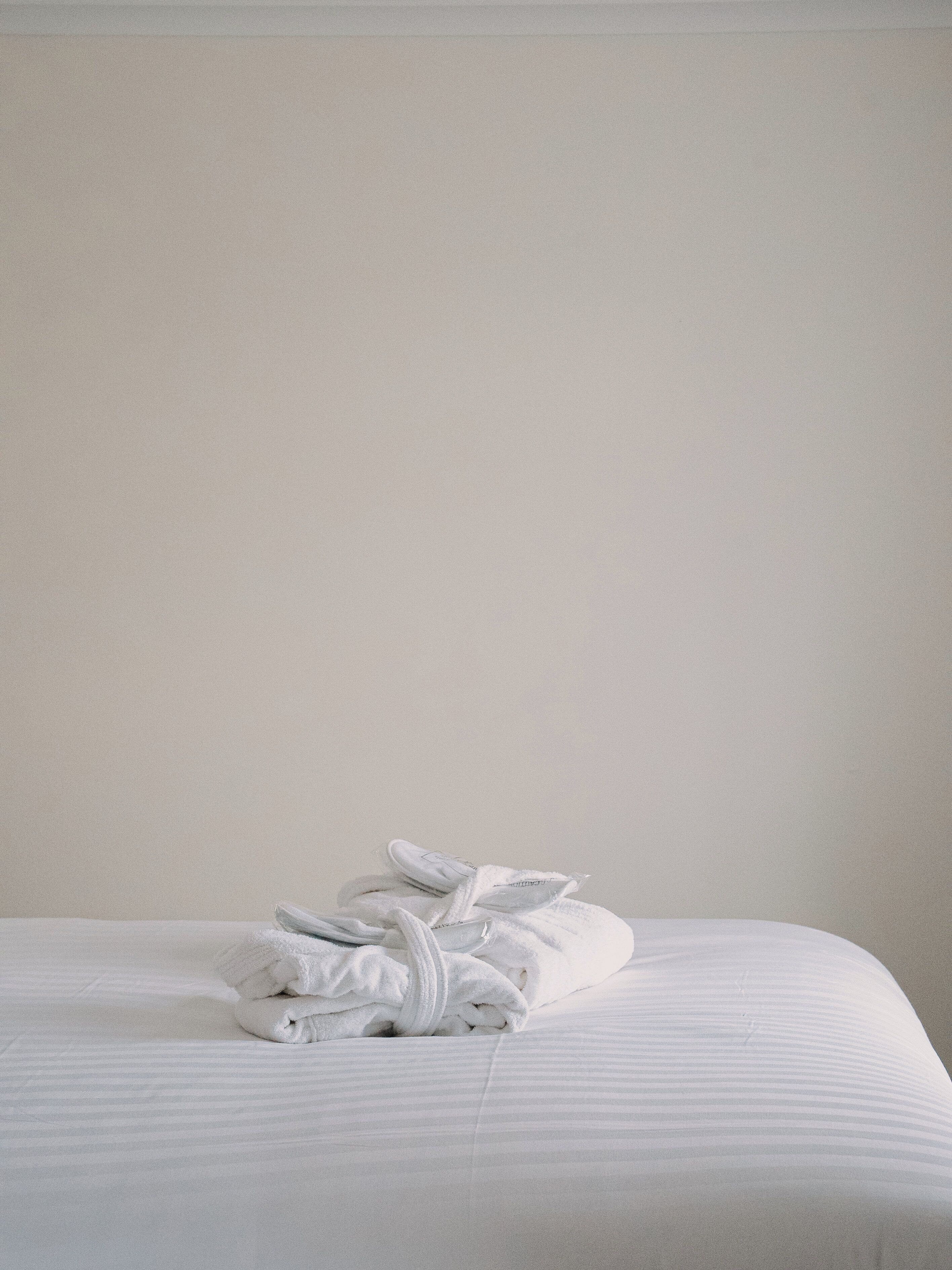 Una cama bien hecha con una toalla blanca doblada y un par de pantuflas blancas encima.