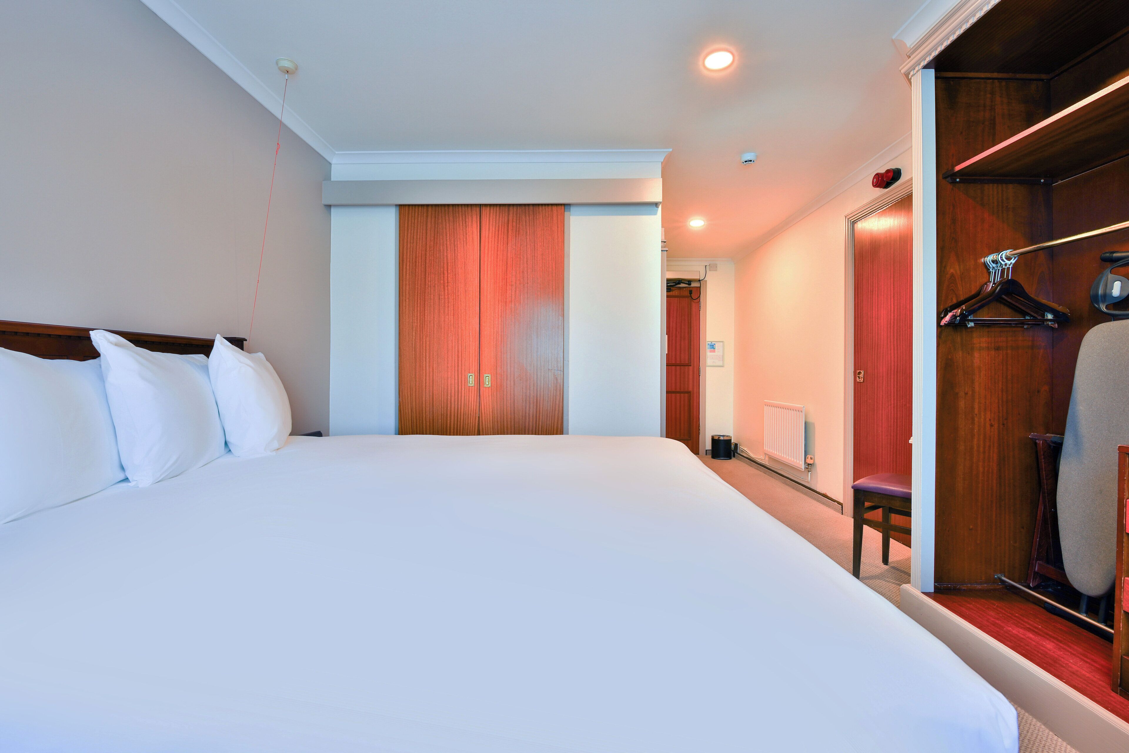 Habitación de hotel con una cama grande, un armario de madera y una zona de estar con una silla y una mesa.