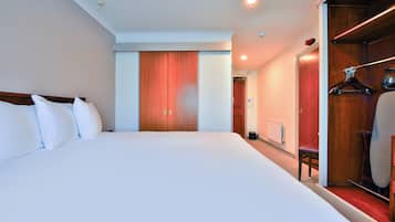 Habitación de hotel con una cama grande, un armario de madera y una zona de estar con una silla y una mesa.