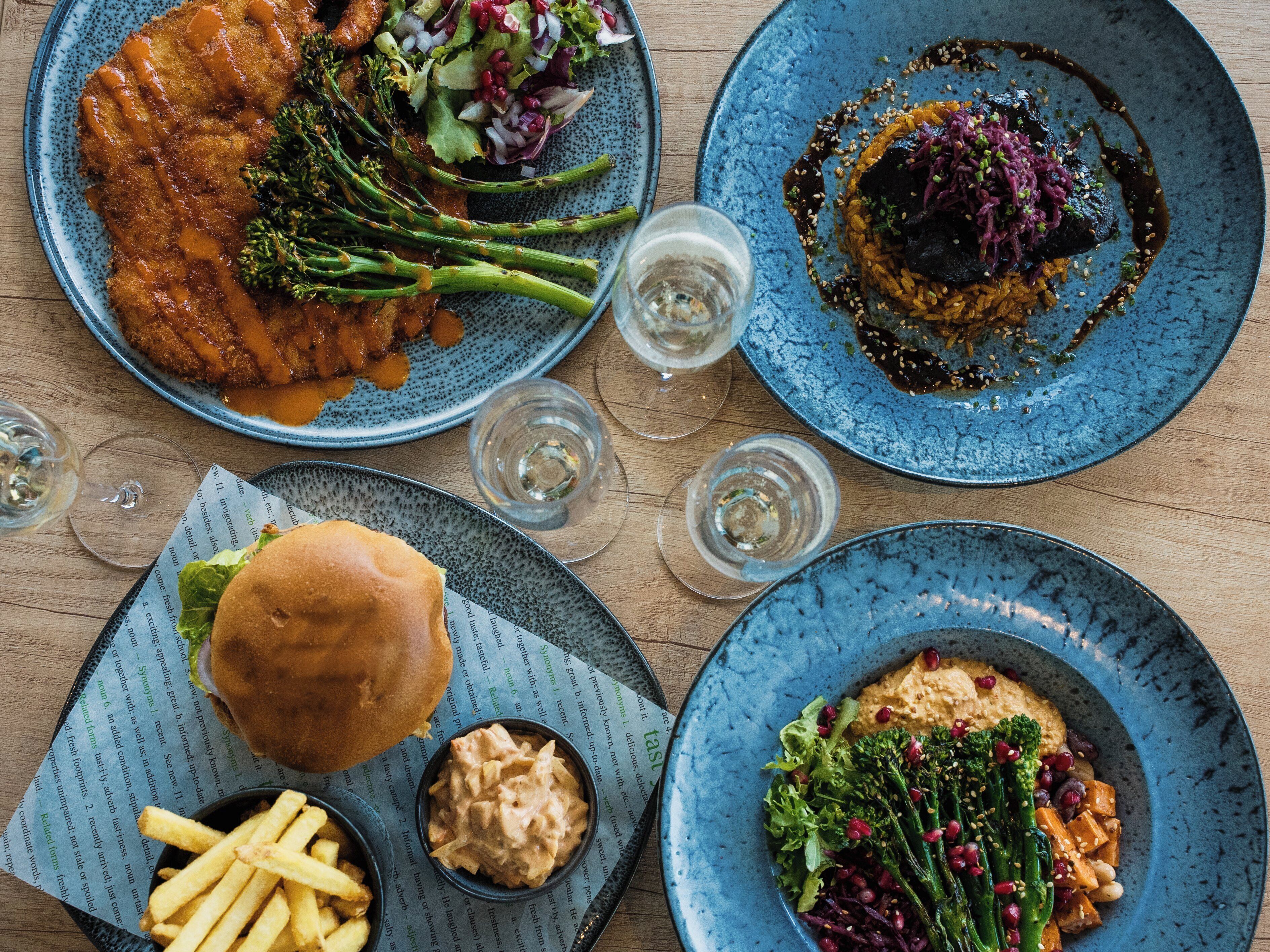 A table with various dishes including a burger, fries, and multiple plates of food.