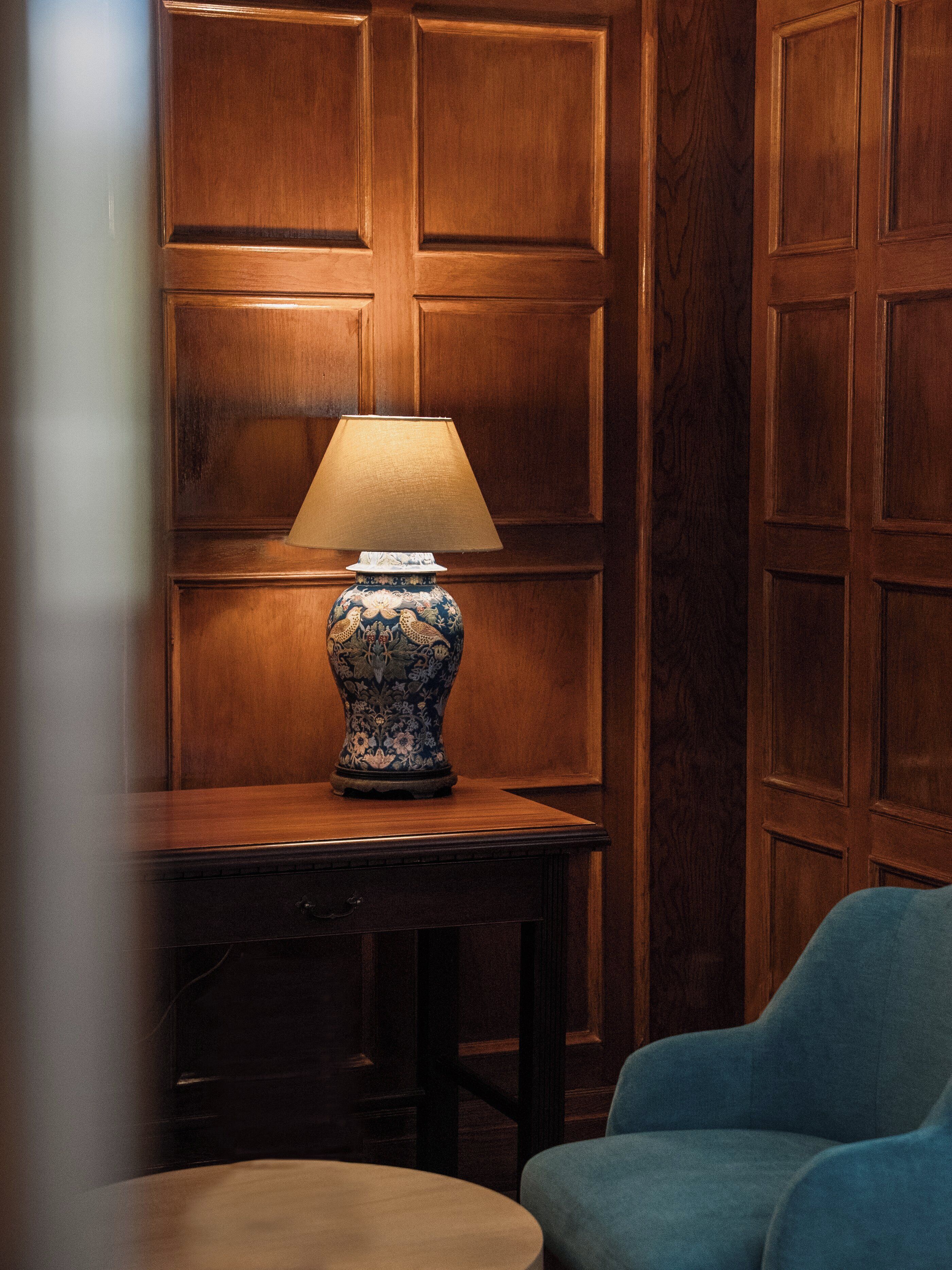 A wooden paneled wall, a table with a lamp, and a blue chair.