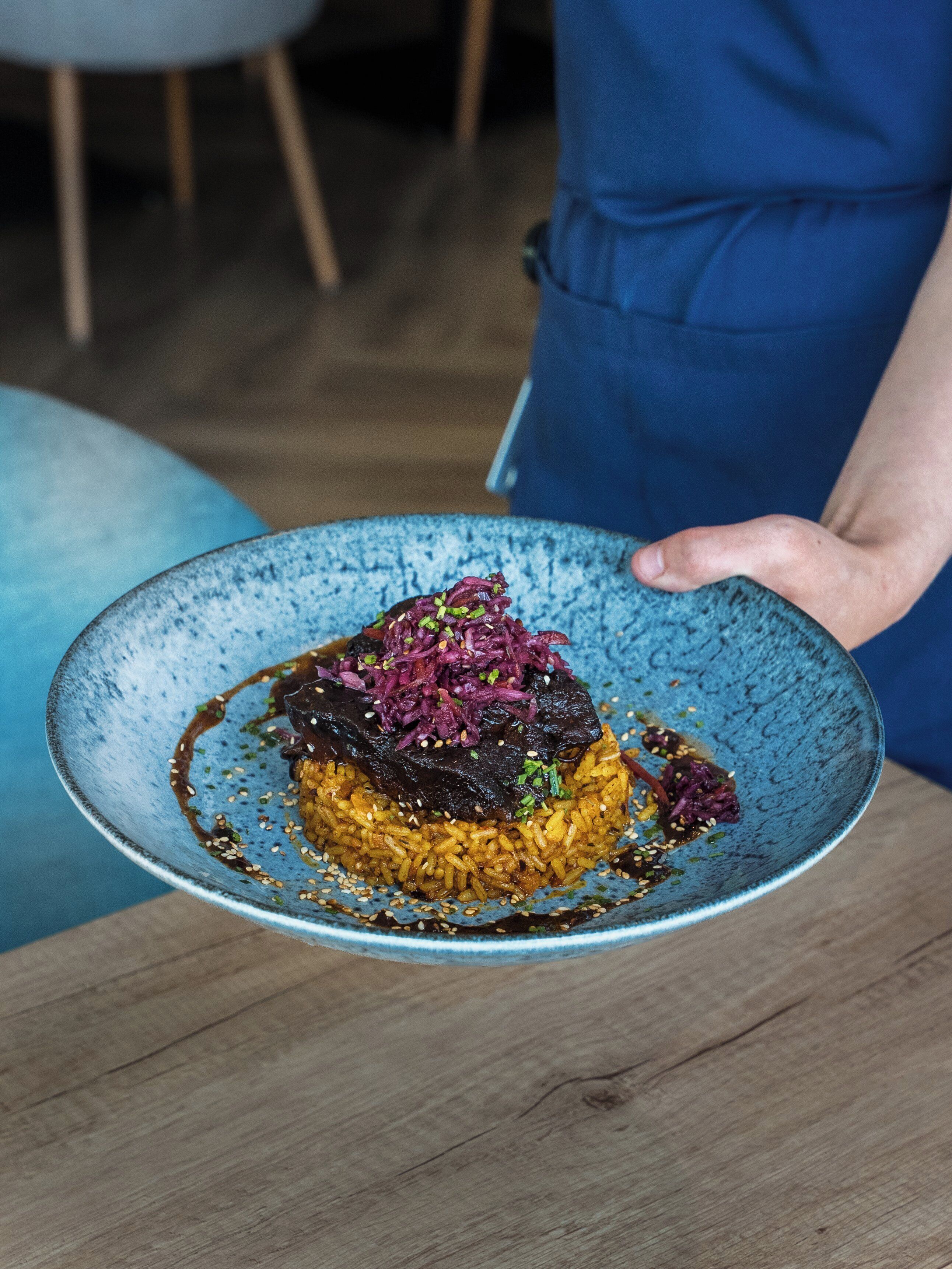 A person holding a blue ceramic plate with a dish of rice, meat, and purple vegetables.