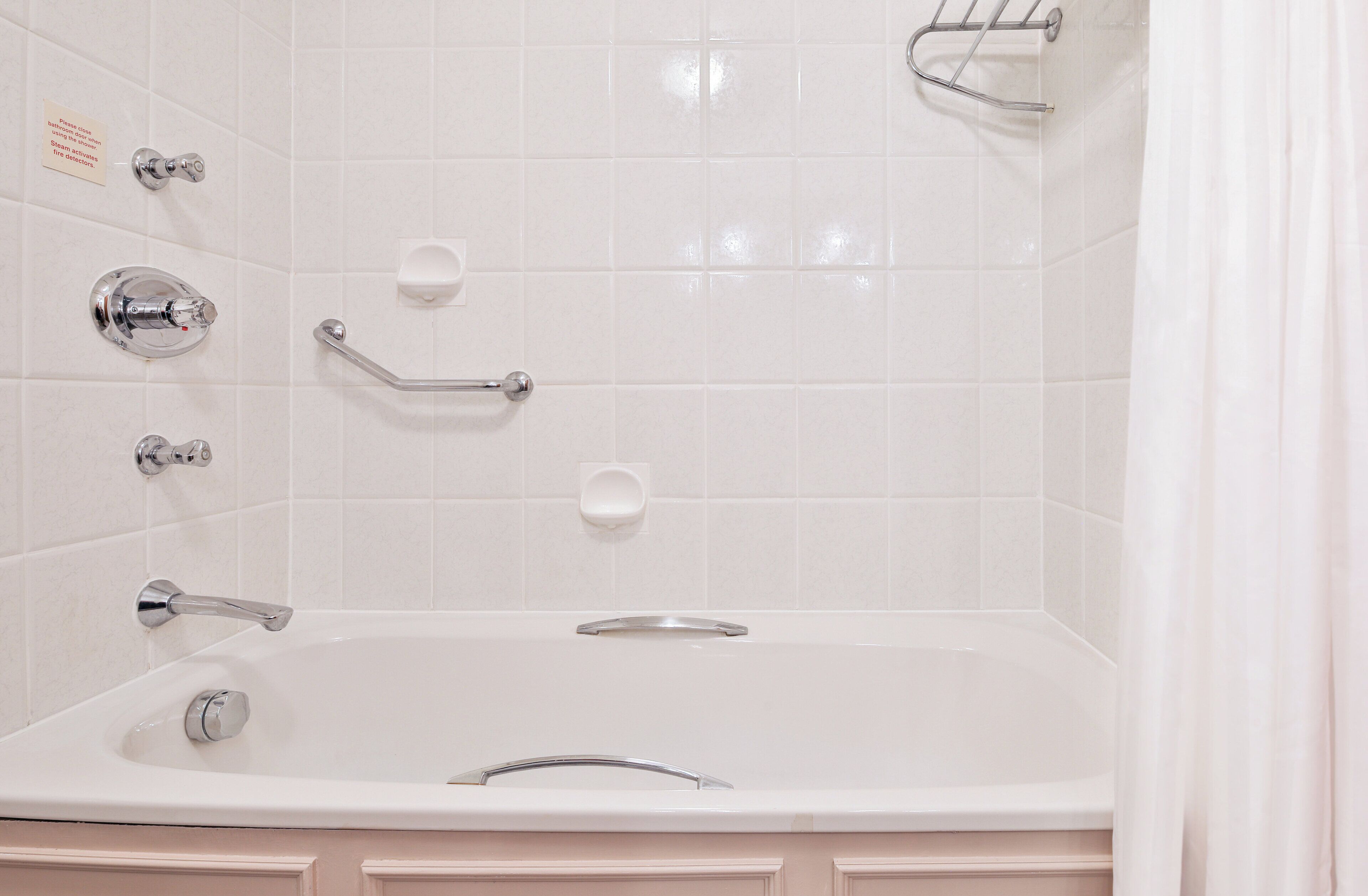 Un baño blanco con bañera, pasamanos y jabonera.