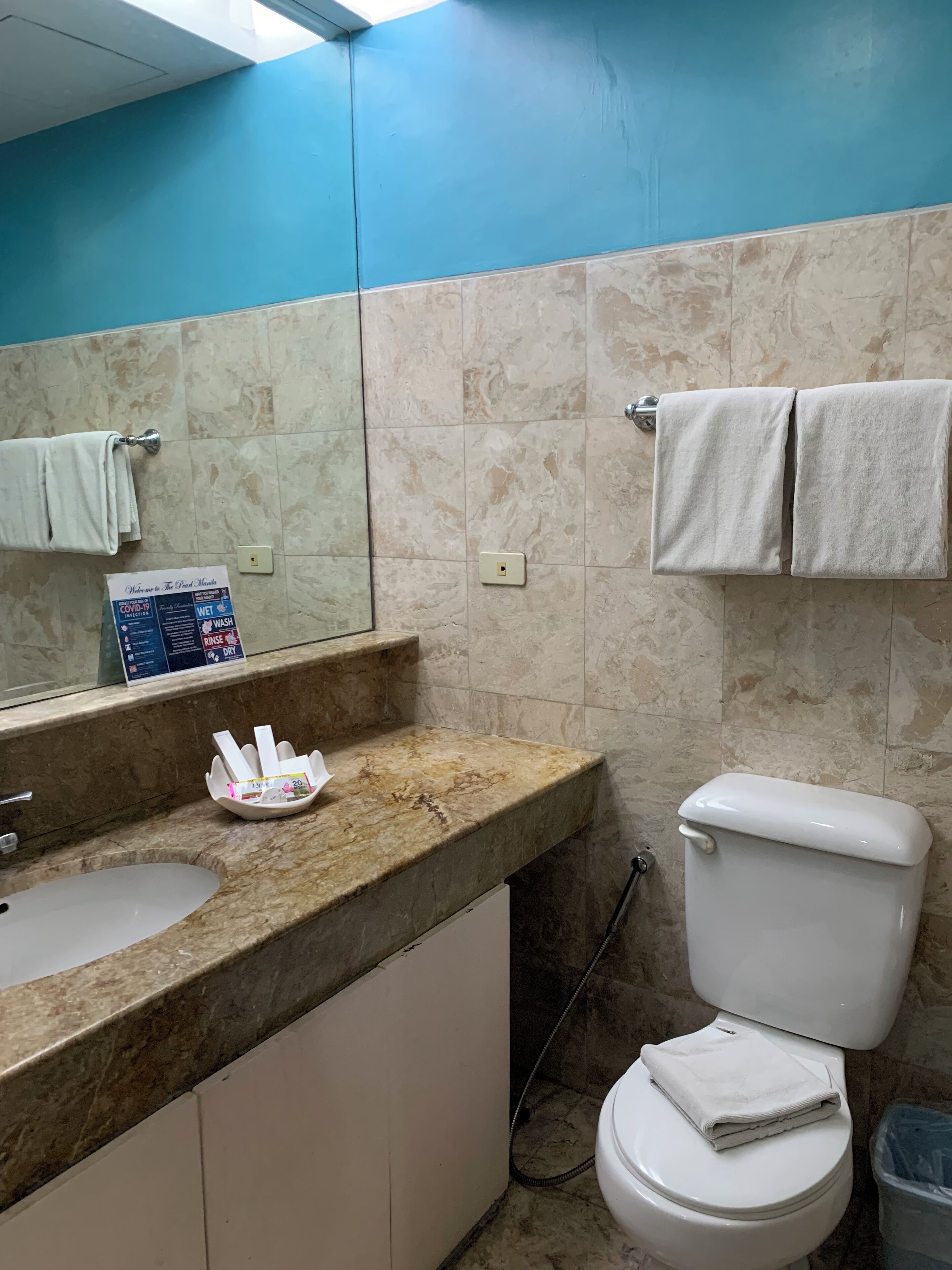 A bathroom with a marble countertop, a sink, a toilet, and a mirror.