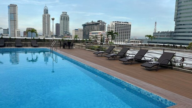 A rooftop pool with lounge chairs and a city skyline in the background. - The Pearl Manila Hotel (Manila)