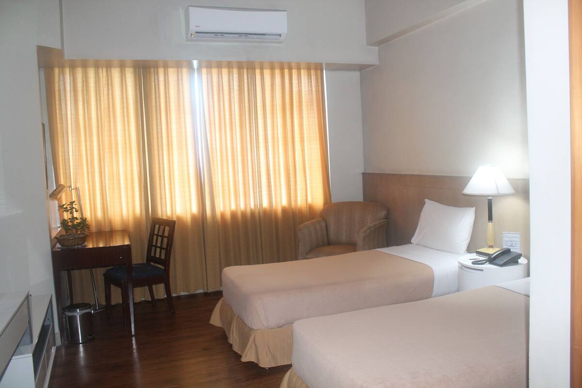 A hotel room with two beds, a desk with a chair, a lamp, and a telephone.