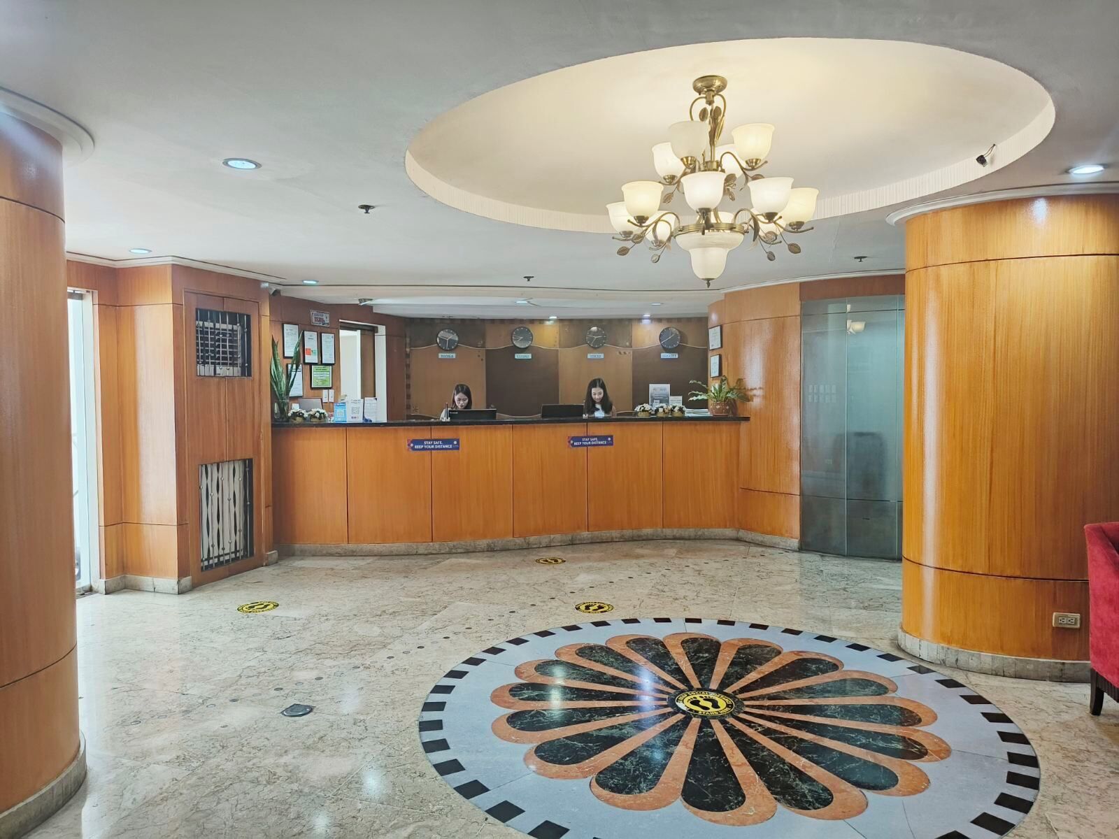 Ein Hotel-Empfangsbereich mit einem Holzbüro, einer Chandelüster, einer Uhr und einem gemusterten Boden.