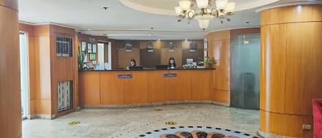 Ein Hotel-Empfangsbereich mit einem Holzbüro, einer Chandelüster, einer Uhr und einem gemusterten Boden.