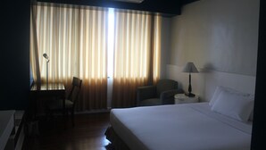 A hotel room with a bed, a desk, a chair, a lamp, and curtains. - The Pearl Manila Hotel (Manila)