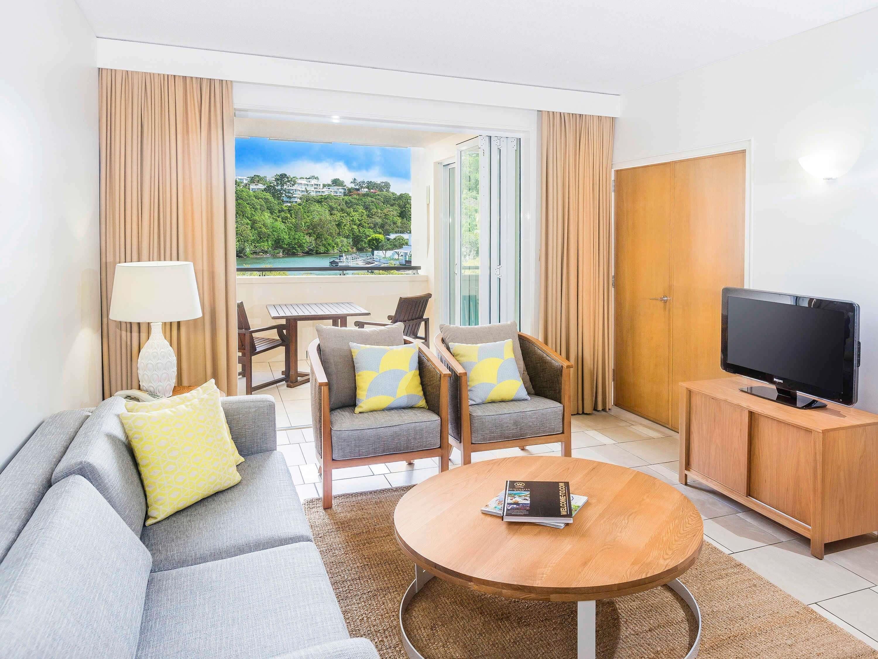 A modern hotel room with a sofa, armchairs, a TV, and a view of a lake.