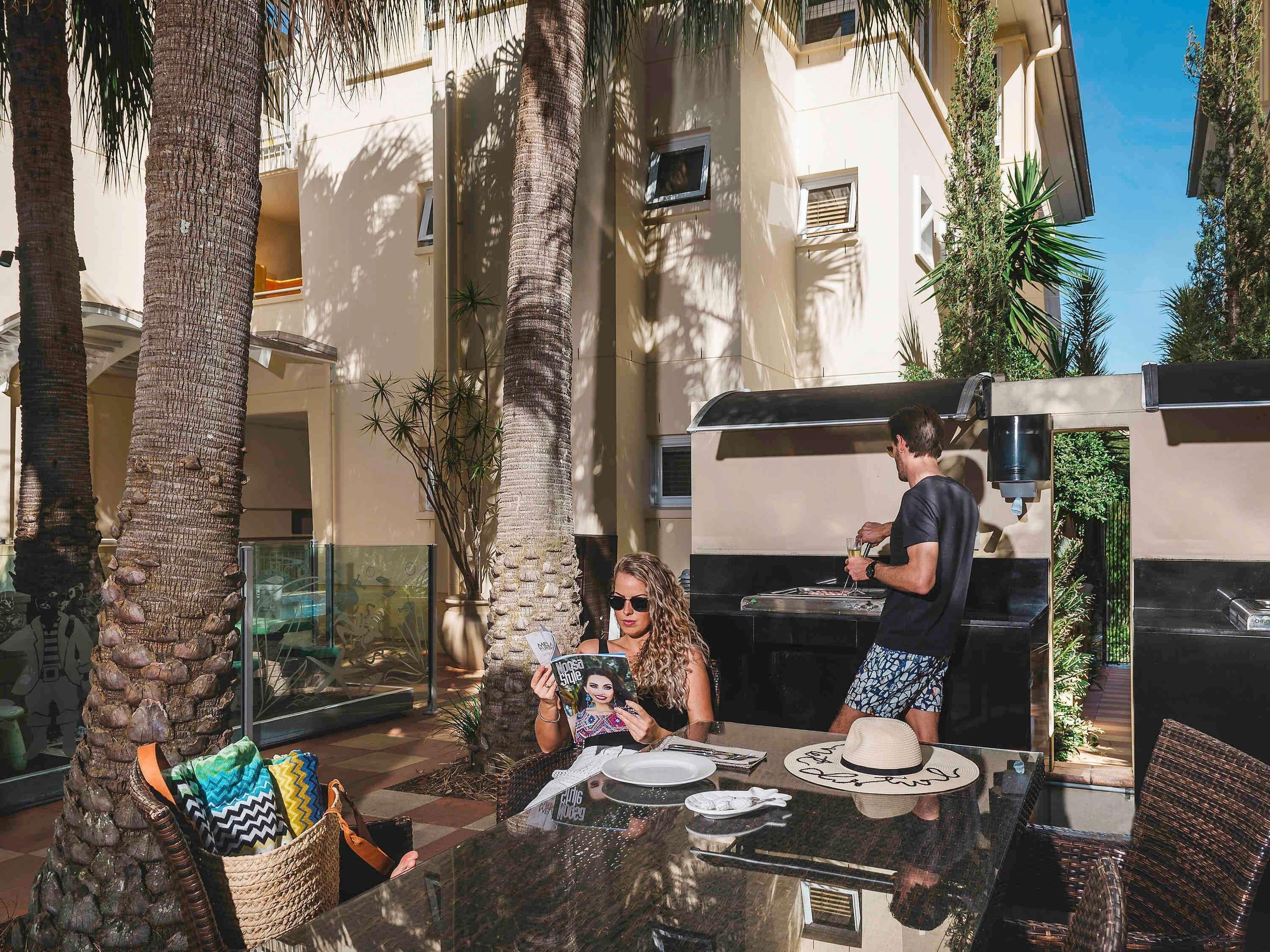 Eine Terrassenanlage im Freien mit Grill, Sitzgelegenheiten und Palmen.