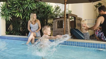 Une piscine avec un toboggan, entourée de verdure et dotée d’un espace ombragé.