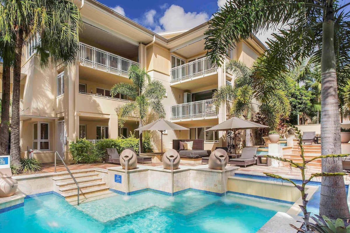 A hotel with a pool, outdoor seating, and palm trees.