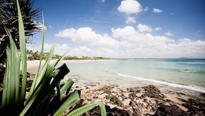 A beach with clear turquoise water, a rocky shoreline, and palm trees. - The Sebel Noosa (Noosa Heads)