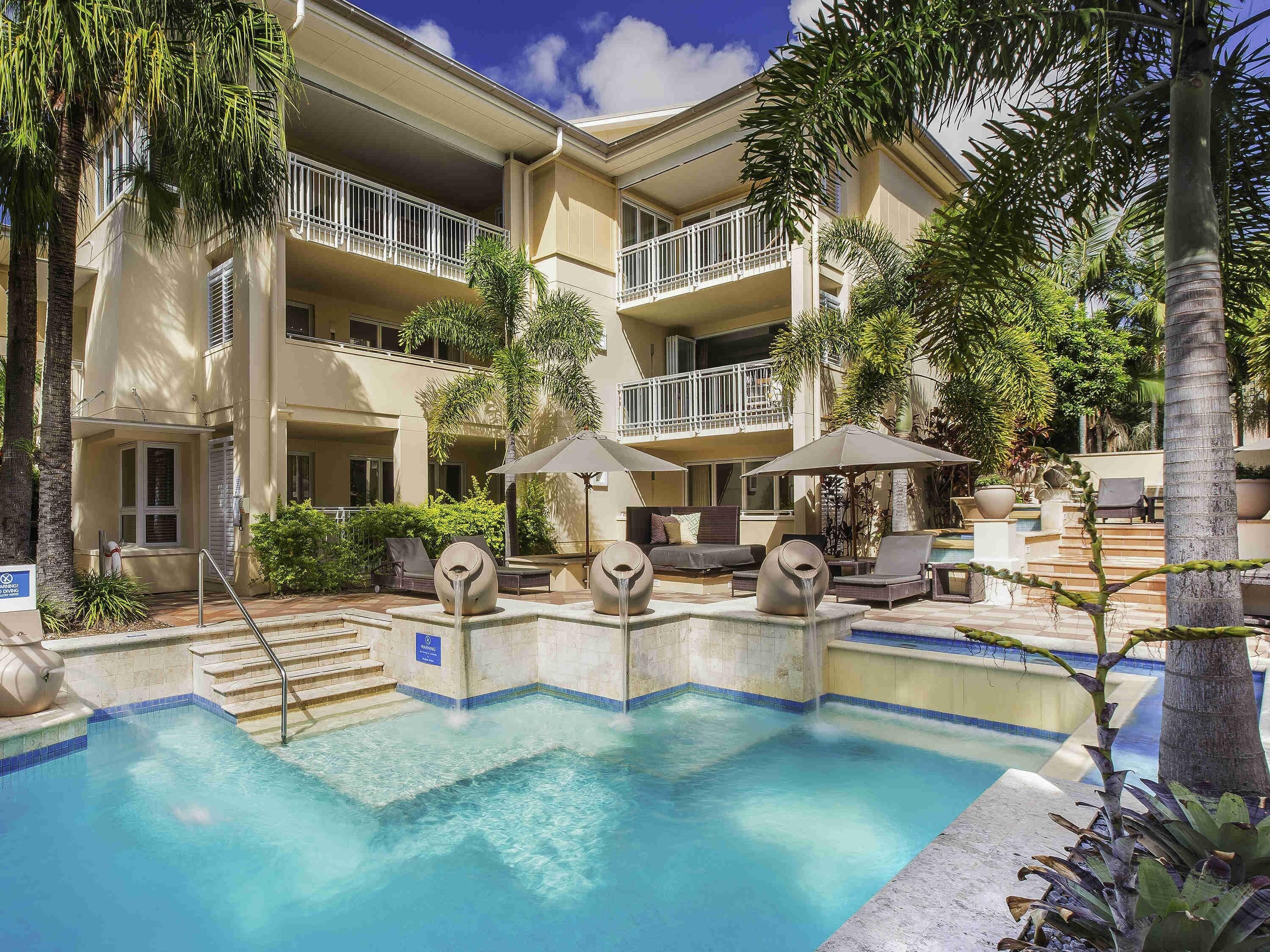 Un hotel con piscina, mobiliario exterior y palmeras.