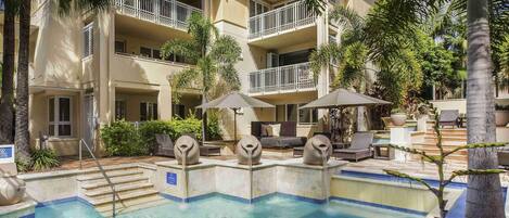 Un hotel con piscina, mobiliario exterior y palmeras.