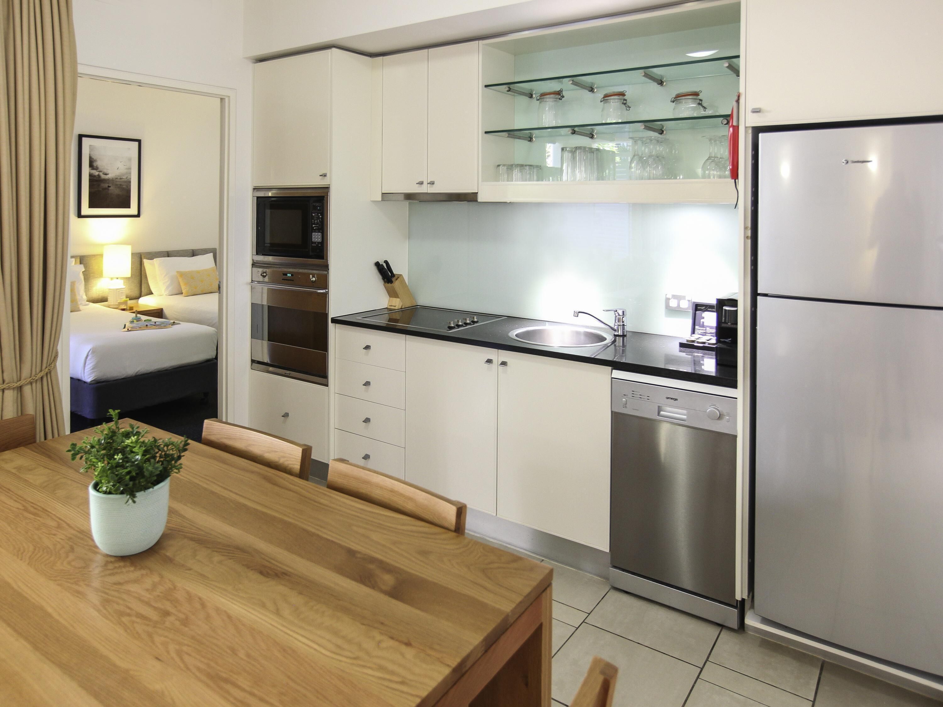 A modern kitchen with stainless steel appliances, a glass-fronted cabinet, and a dining area with a wooden table and chairs.