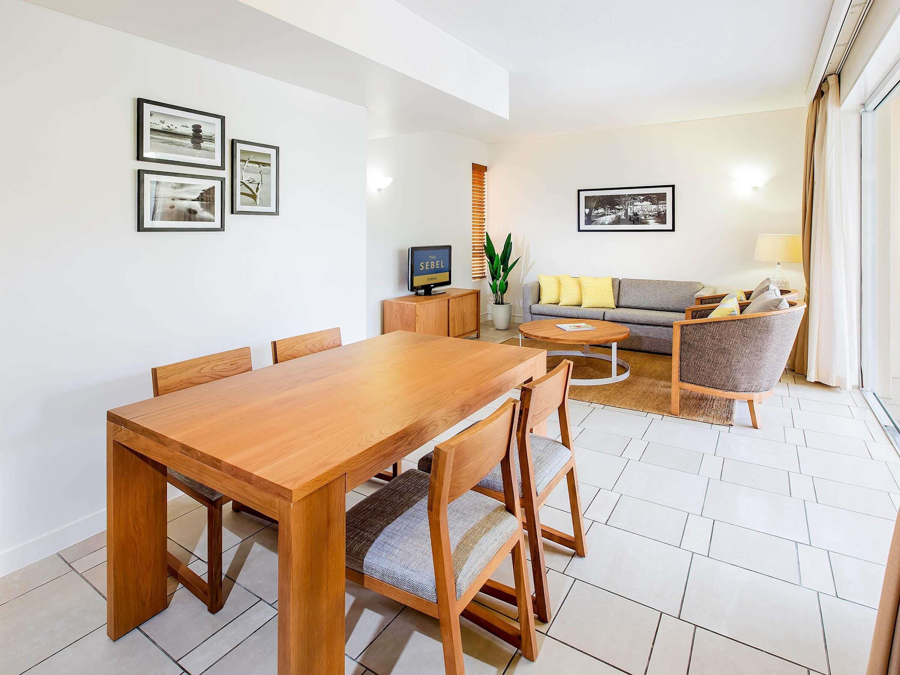 A modern living room with a wooden dining table, a sofa, and a TV.