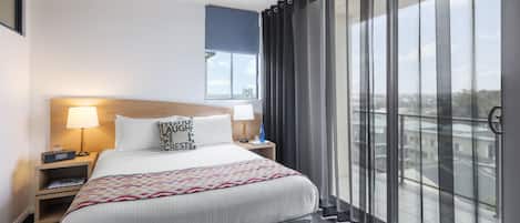 Habitación de hotel con una cama grande, dos mesitas de noche, una ventana con cortinas y vista a la ciudad.