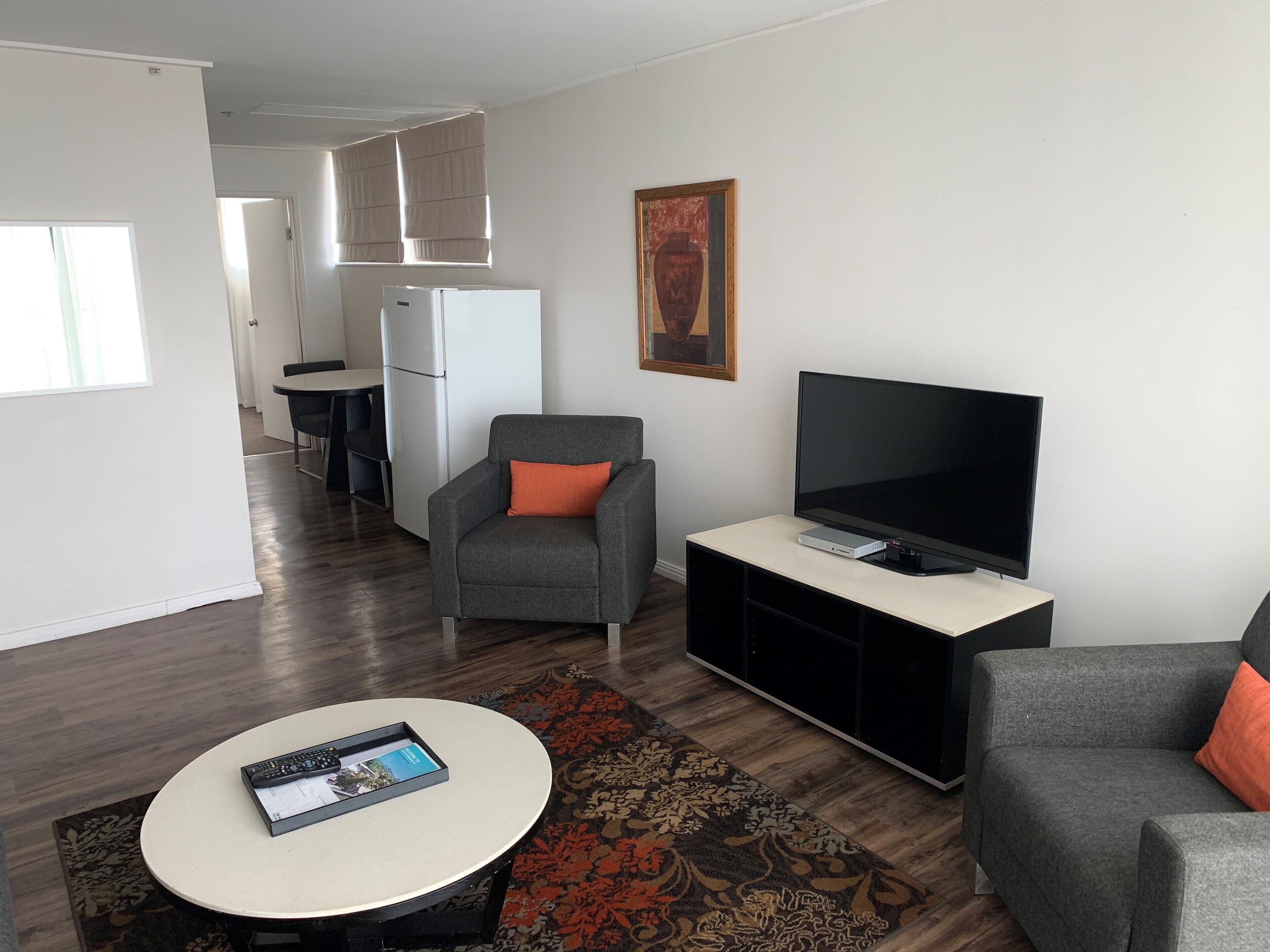 A modern living room with a grey sofa, a television, a small table with a remote control, and a patterned rug.