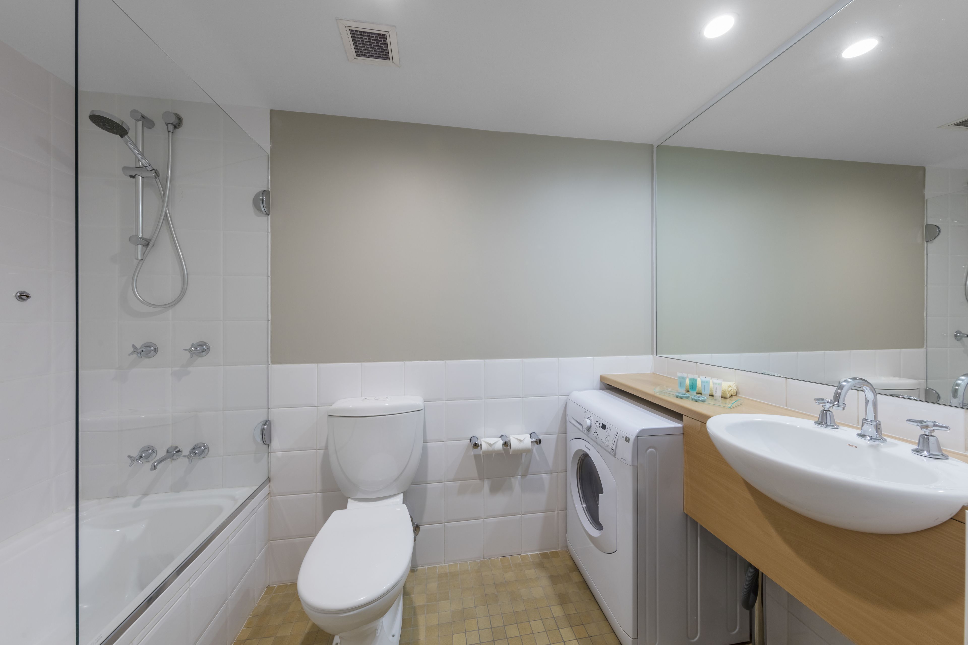 Un bagno moderno con doccia vetrata, un WC, una lavatrice e un lavandino con specchio sopra.