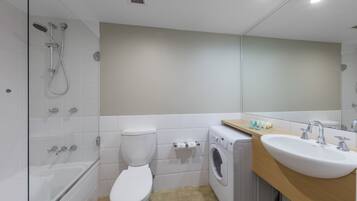 Un bagno moderno con doccia vetrata, un WC, una lavatrice e un lavandino con specchio sopra.