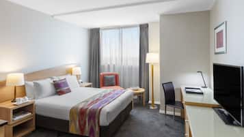 A hotel room with a bed, bedside tables, a desk with a chair, a TV, and a window with curtains.