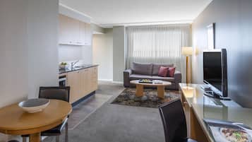 A modern hotel room with a kitchenette, a dining area, a sofa, and a TV.