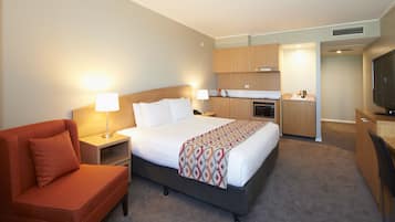 Habitación de hotel con cama, sofá, escritorio, televisor, kitchenette y baño.