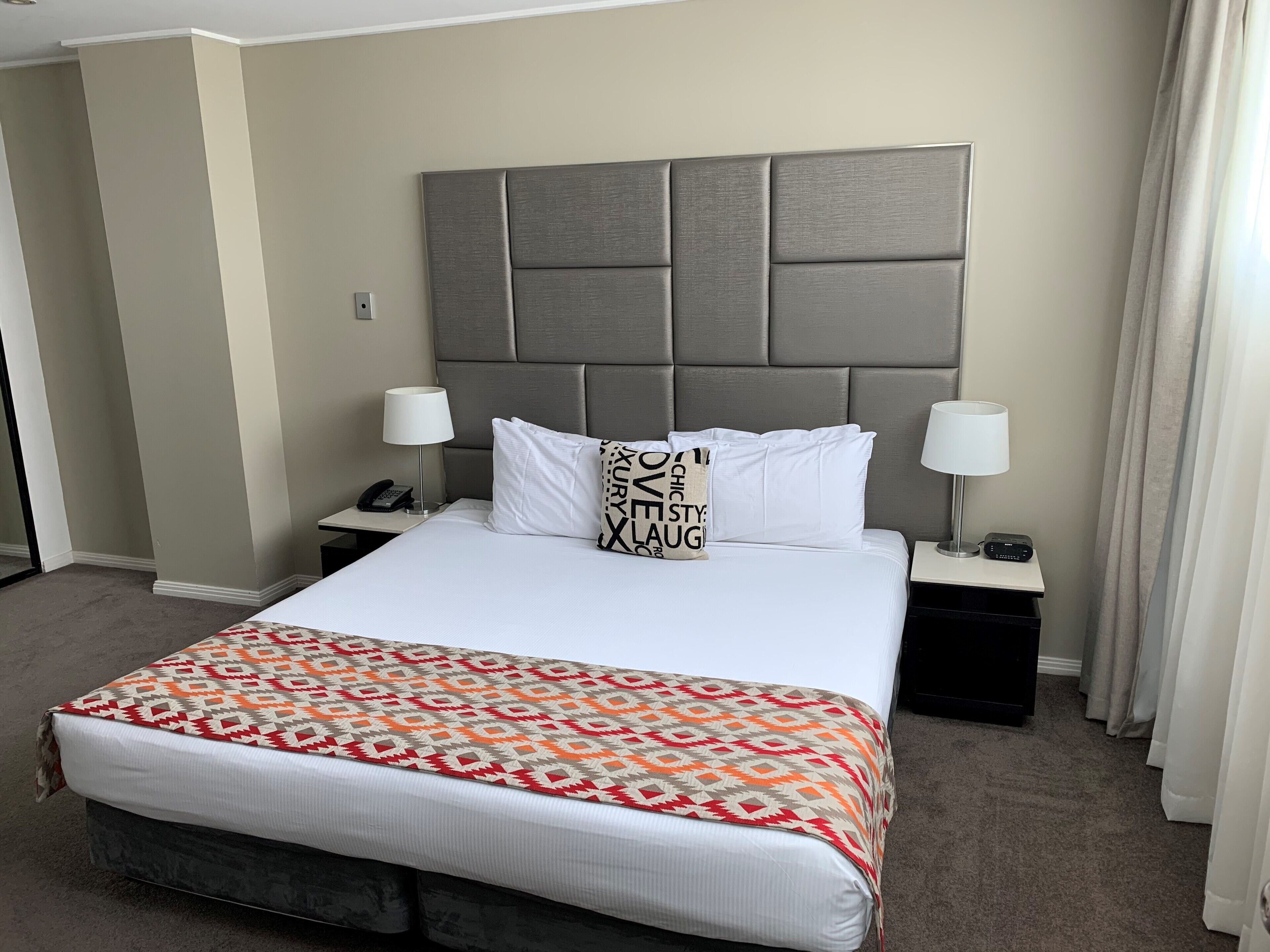 A hotel room with a large bed, two bedside tables, a telephone, and a lamp on each side.