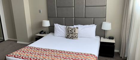 A hotel room with a large bed, two bedside tables, a telephone, and a lamp on each side.