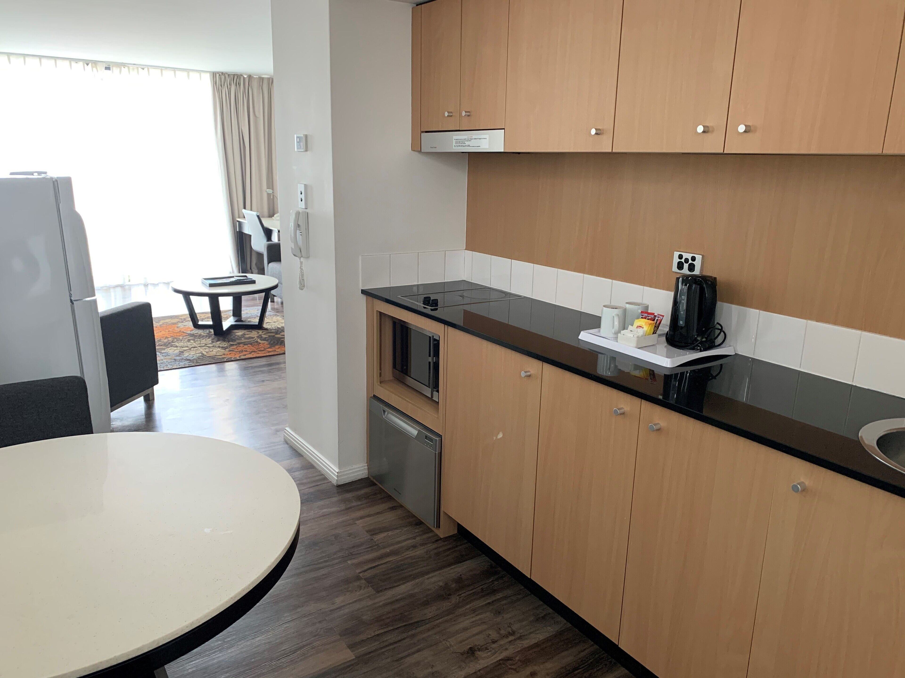 A modern kitchen with wooden cabinets, a black countertop, and a built-in microwave. There is a small dining area with a round table and chairs.