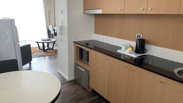 A modern kitchen with wooden cabinets, a black countertop, and a built-in microwave. There is a small dining area with a round table and chairs.