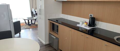 A modern kitchen with wooden cabinets, a black countertop, and a built-in microwave. There is a small dining area with a round table and chairs.