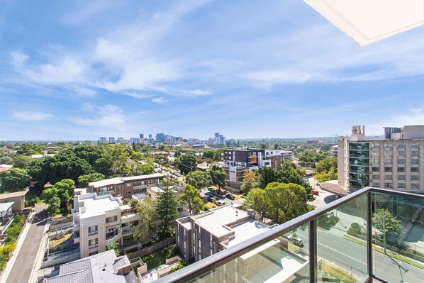 A high-rise building with a glass balcony overlooking a cityscape with various buildings and greenery. - Nesuto Parramatta (Rosehill)